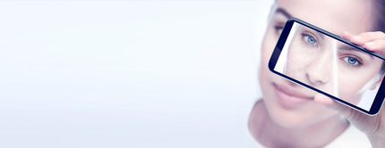 A close-up of a woman's face as she holds a smartphone displaying a digital overlay of a facial recognition grid on her eye, against a soft gradient background.