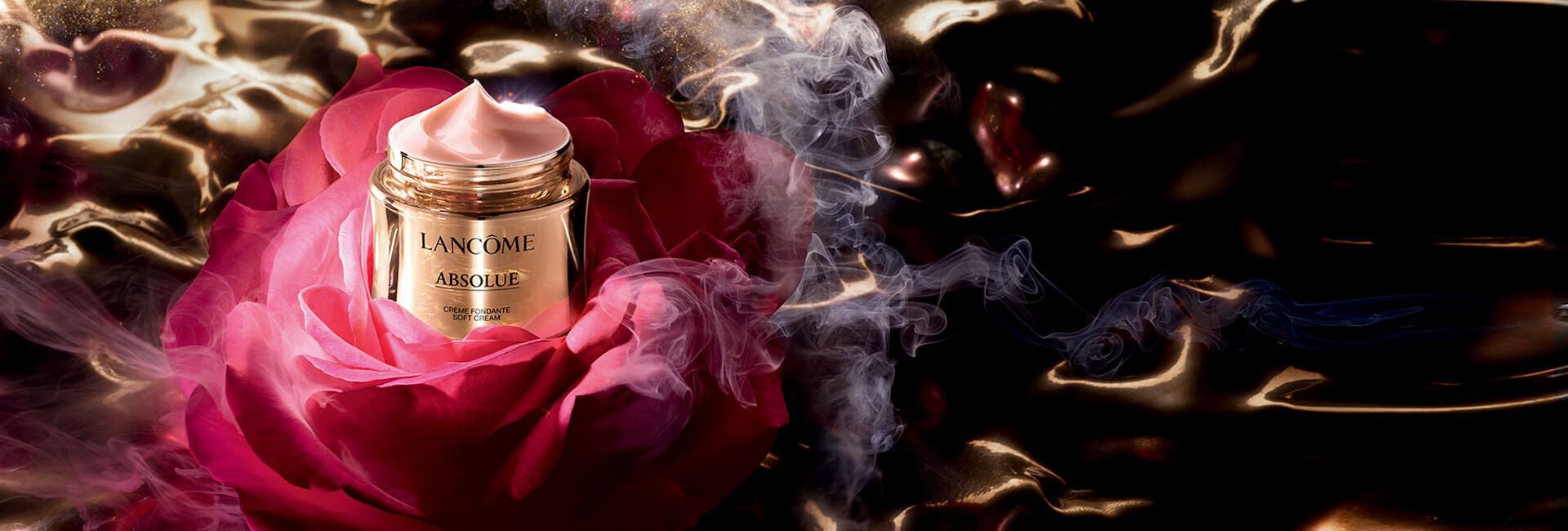 A luxurious jar of Lancome Absolue cream sits atop a vibrant rose, surrounded by swirling smoke and a dark, glossy background, evoking a sense of elegance and indulgence.