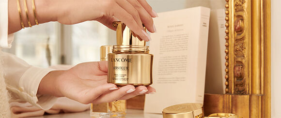 Une main tenant un pot de creme de luxe Lancome Absolue, avec un decor elegant en arriere-plan.