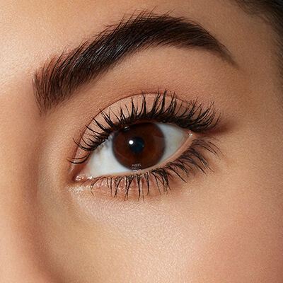 Close-up of a human eye with dark brown iris, long eyelashes, and well-defined eyebrows. The skin around the eye appears smooth and lightly makeup-enhanced.