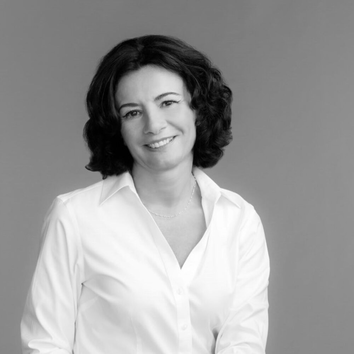 Zwart-witportret van een vrouw met krullend haar in een witte blouse, die glimlacht naar de camera.
