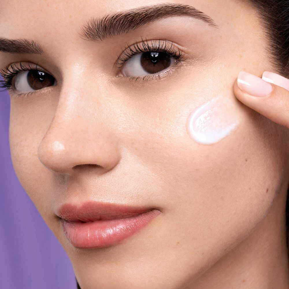 Une femme applique une creme hydratante sur son visage, mettant en valeur son teint eclatant et ses traits harmonieux.
