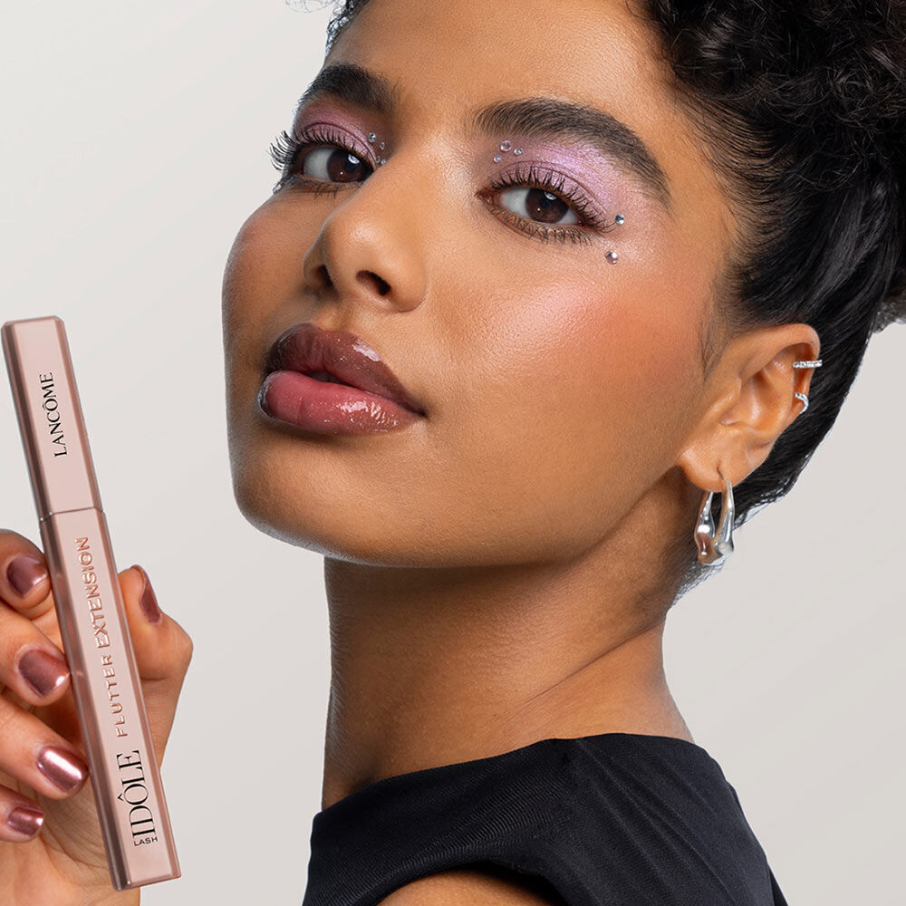 Une femme avec un maquillage eclatant, tenant un mascara Lancome, posant avec confiance.