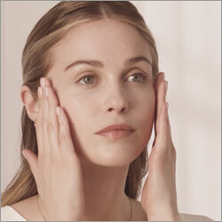 A young woman with long, straight hair is gently massaging her face with her hands, showcasing a natural and fresh look.