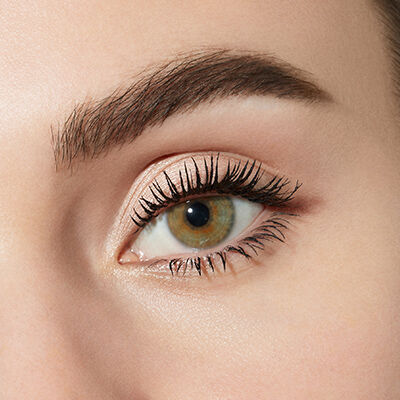 Close-up of a human eye showing long eyelashes, a smooth eyelid with subtle makeup, and a brown iris.