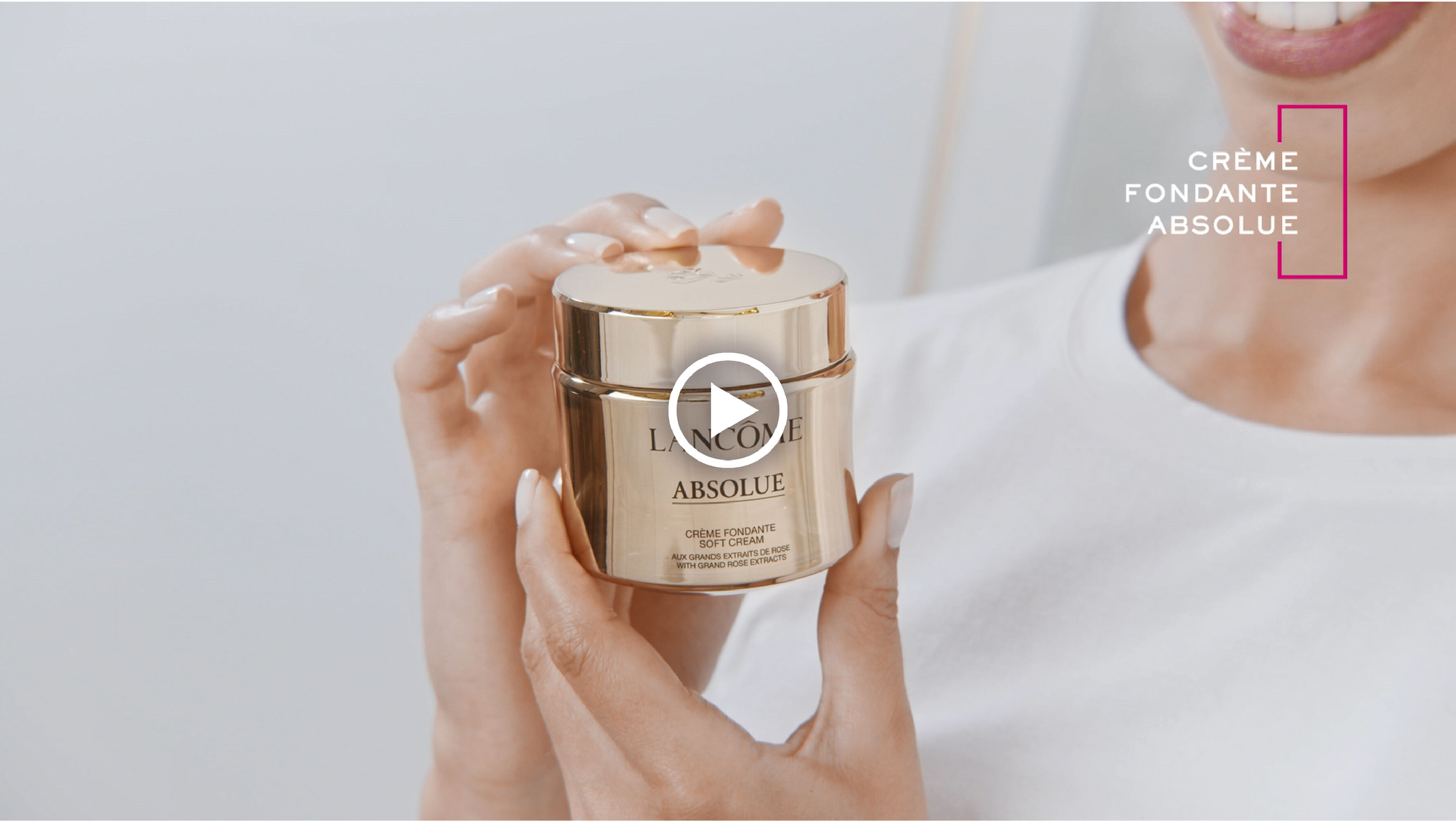 Une femme souriante montre un pot de creme Lancome, 'Creme Fondante Absolue', sur fond neutre.