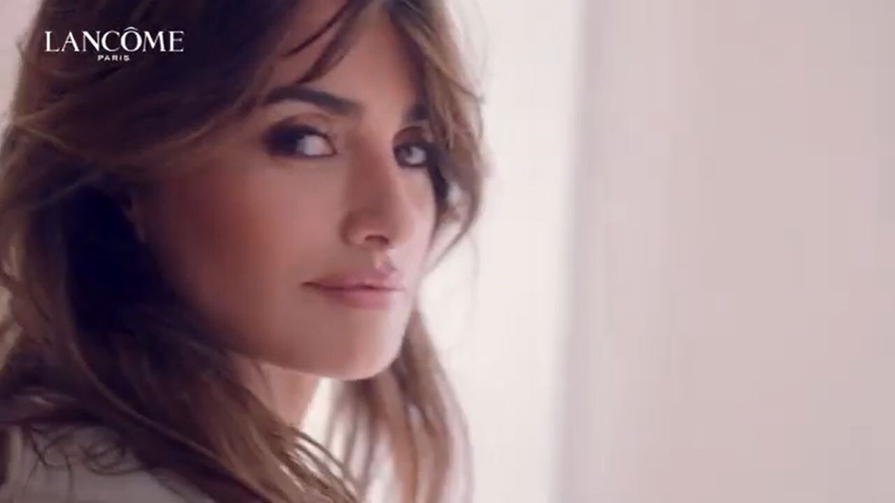 Femme au regard captivant, posant avec elegance, mise en valeur par une lumiere douce. Logo Lancome en haut a gauche.