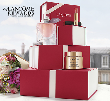 Boites rouges de produits Lancome, accompagnees de fleurs, sur une table avec une vue de la ville en arriere-plan.