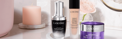 Produits de beaute Lancome, incluant un serum, un fond de teint et une creme, presentes sur une surface elegante avec une bougie.