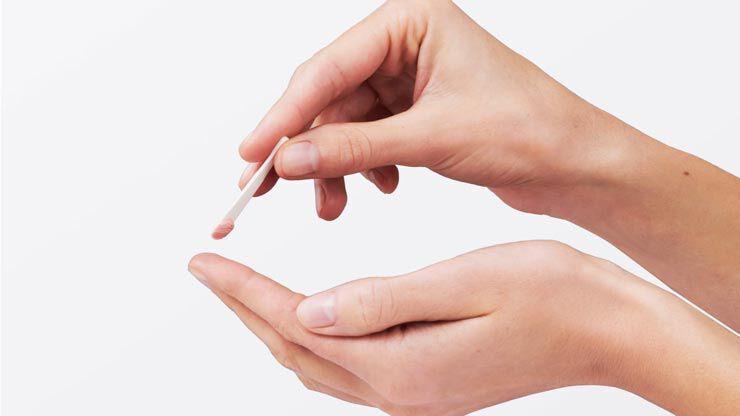 Une main tient un batonnet appliquant une creme ou un produit sur la paume de l'autre main.