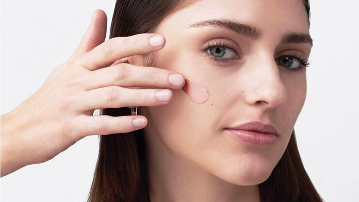 Une femme maquille sa joue avec un produit de beaute, regardant la camera.