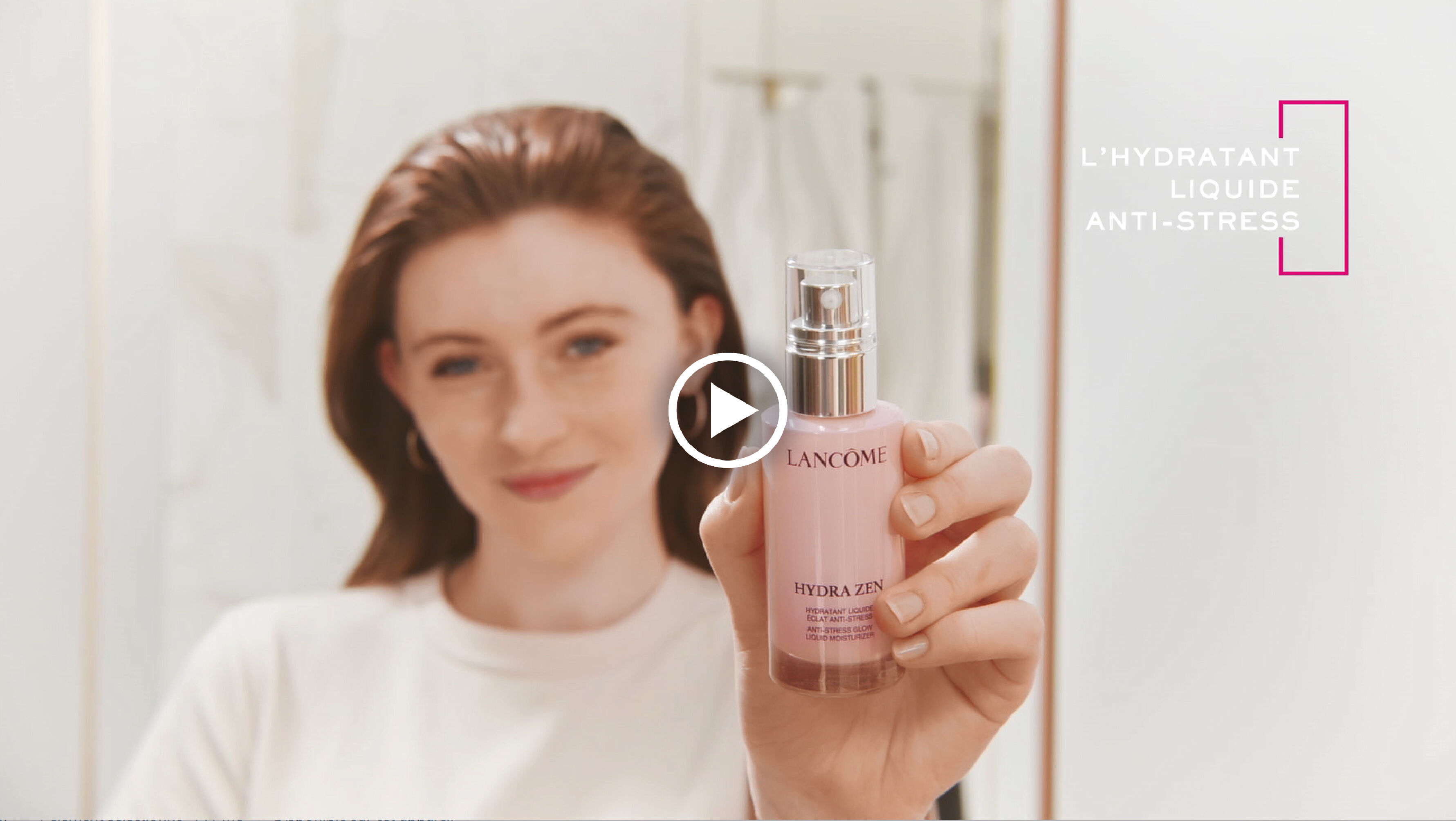 Une femme souriante tient un flacon de serum Hydra Zen de Lancome devant un miroir dans un decor lumineux.