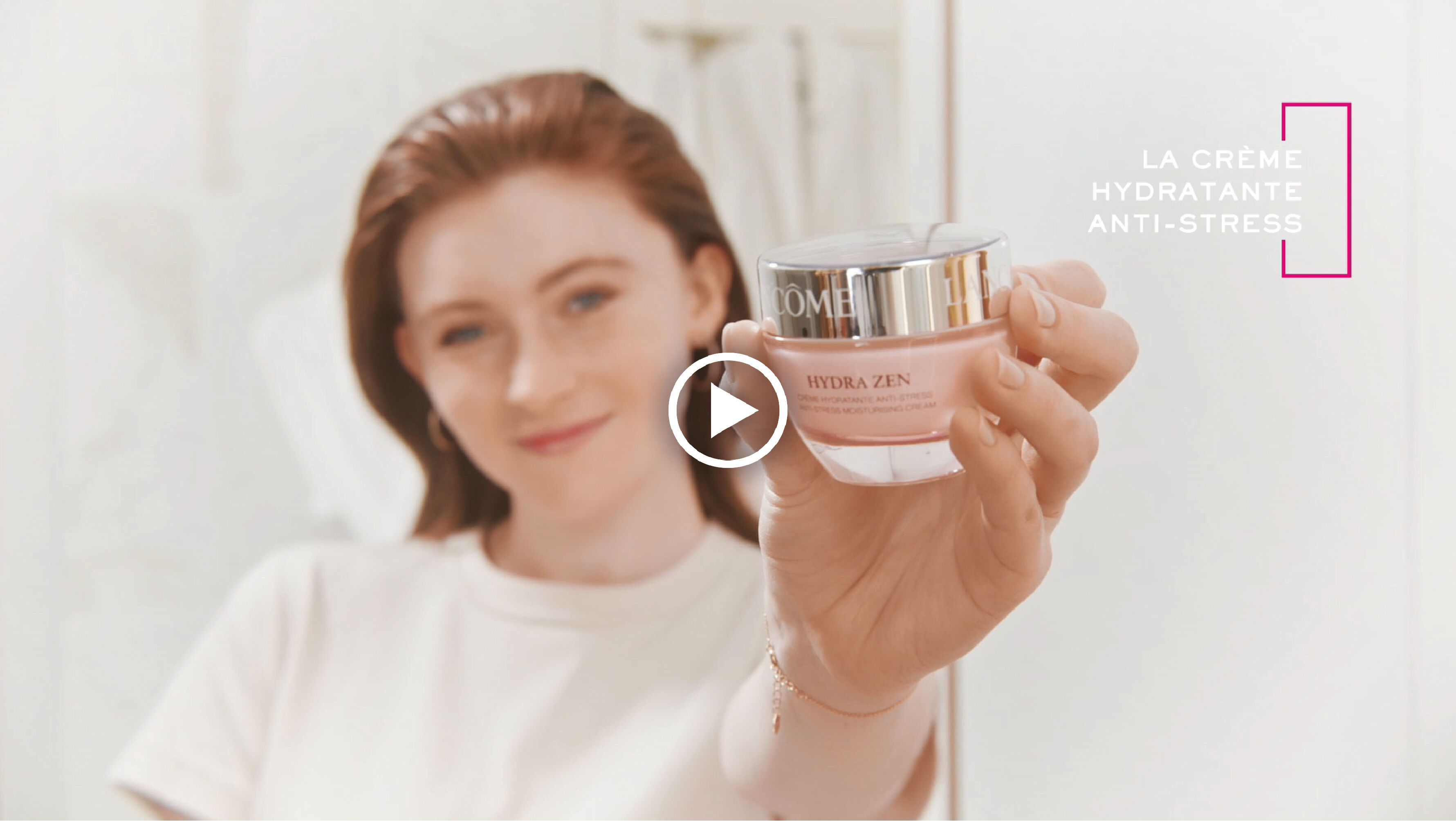 Une jeune femme souriante presente la creme hydratante anti-stress Hydra Zen de Lancome dans une salle de bain lumineuse.