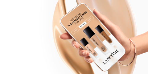 Een hand houdt een smartphone vast met een applicatie van Lancome die verschillende foundation tinten toont, met de tekst "We found the perfect shade for you".