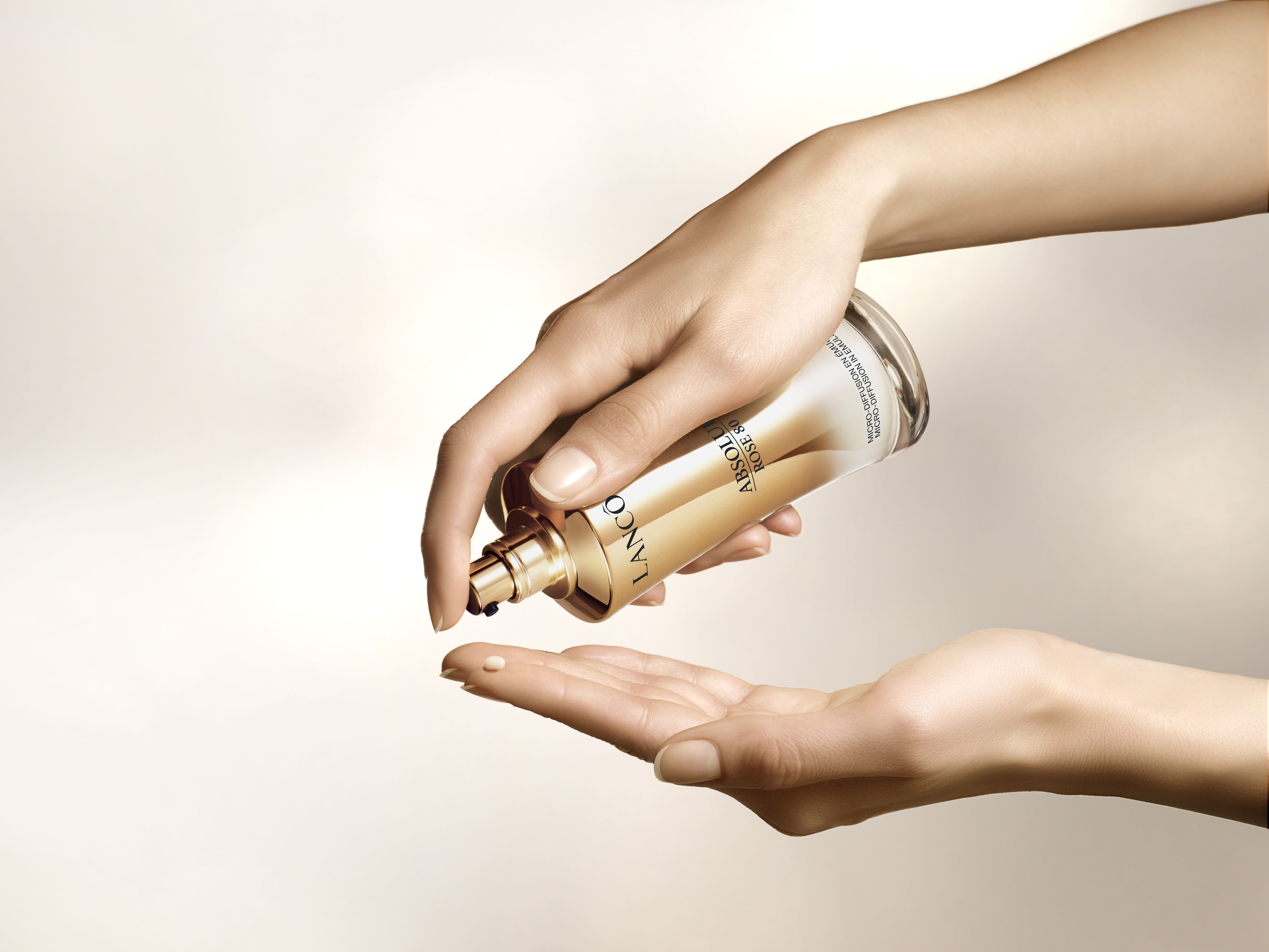 Een hand pompt een sierlijke fles met een luxe huidverzorgingsproduct uit, klaar om aangebracht te worden.