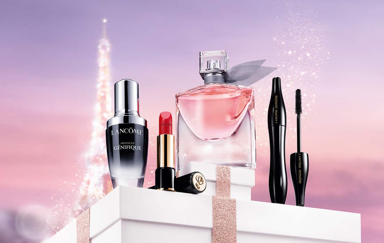 Gamme de produits Lancôme, incluant un sérum, un parfum, un rouge à lèvres et un mascara, sur un fond étoilé.
