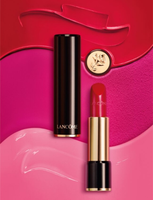Rouge à lèvres Lancôme posé sur un fond coloré de roses et de fuchsias, mettant en avant son éclat vibrant.